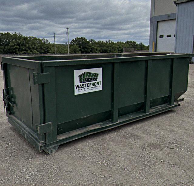 Empty dark green container in a yard beside a warehouse