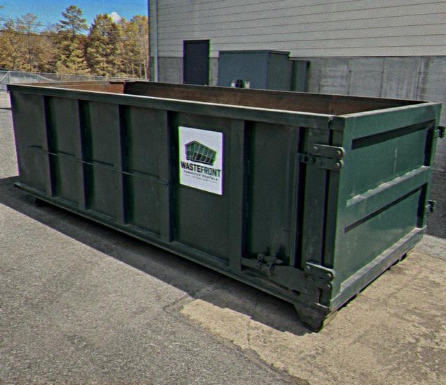 Dark green open-top container set down beside a building