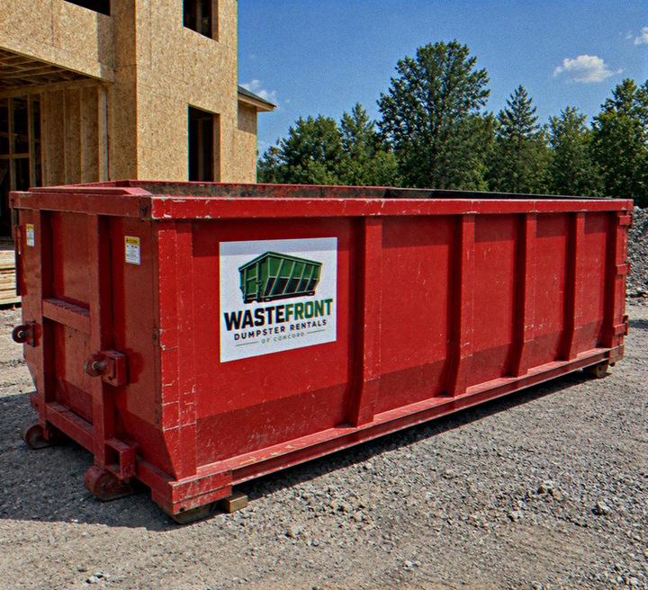 Red roll-off container parked on gravel beside a house under construction
